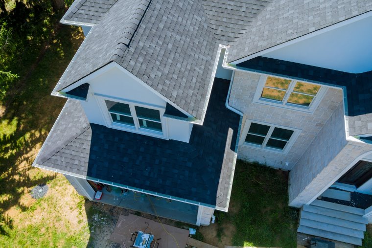Aerial view of newly installed charcoal colored asphalt roof on white home